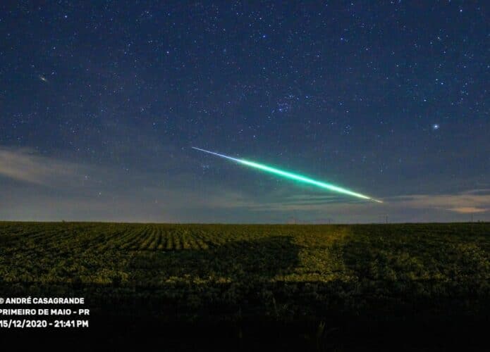 Meteoro de calda azul/verde passando por céu estrelado e campo verde