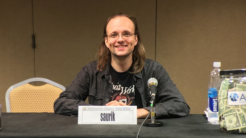 Jay "Saurik" Freeman, criador da Cydia, em uma mesa com um microfone à sua frente