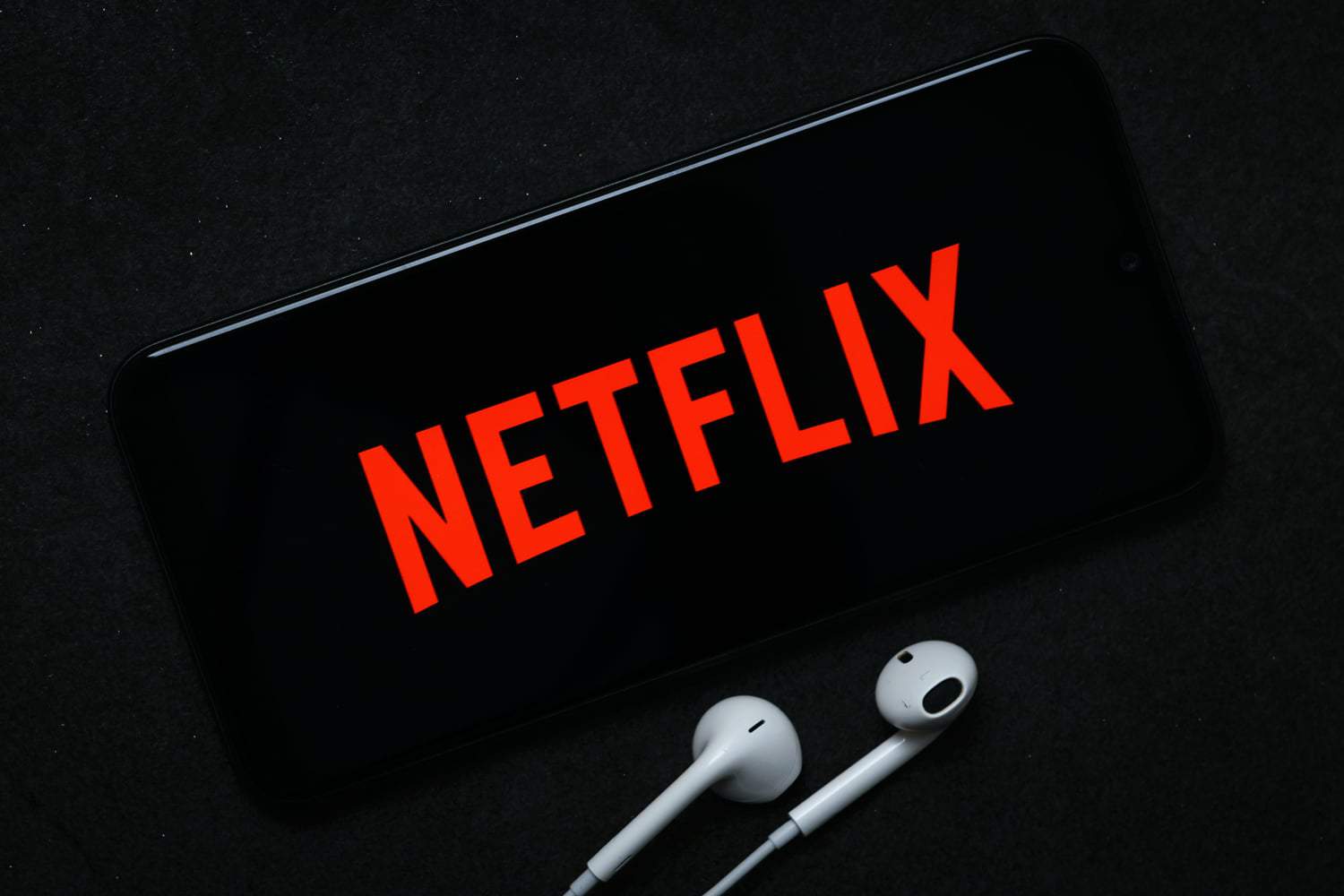Logo da Netflix é exibida em tela de smartphone, com fones de ouvido ao lado do aparelho