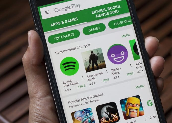 Mão segura smartphone exibindo a tela principal da Google Play