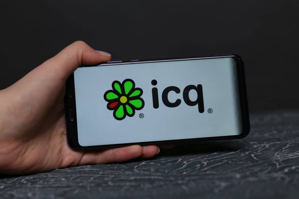 Pessoa segurando celular com logomarca do ICQ