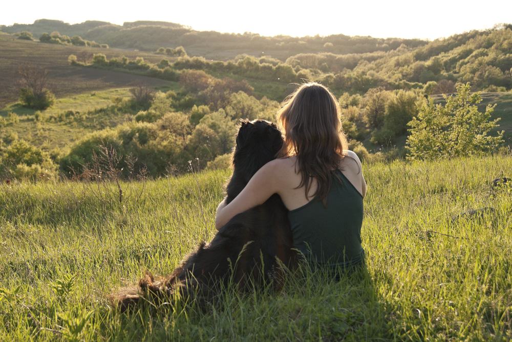 young woman hugs her dog as they sit in a field