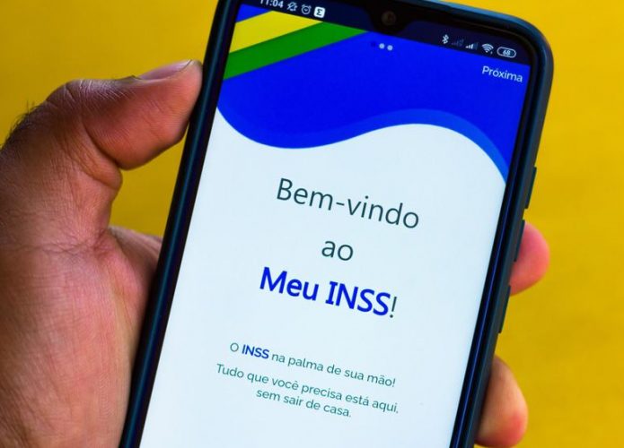 Pessoa segurando celular com aplicativo Meu INSS aberto na tela inicial