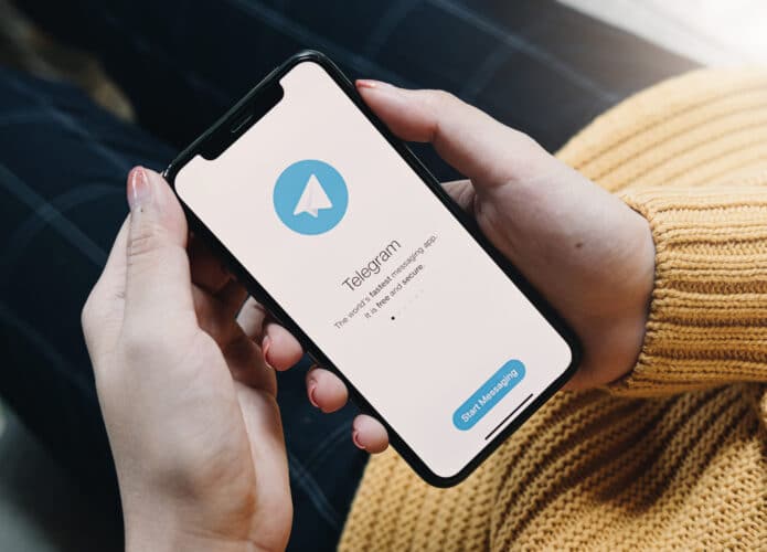 Pessoa segura smartphone exibindo tela inicial do Telegram