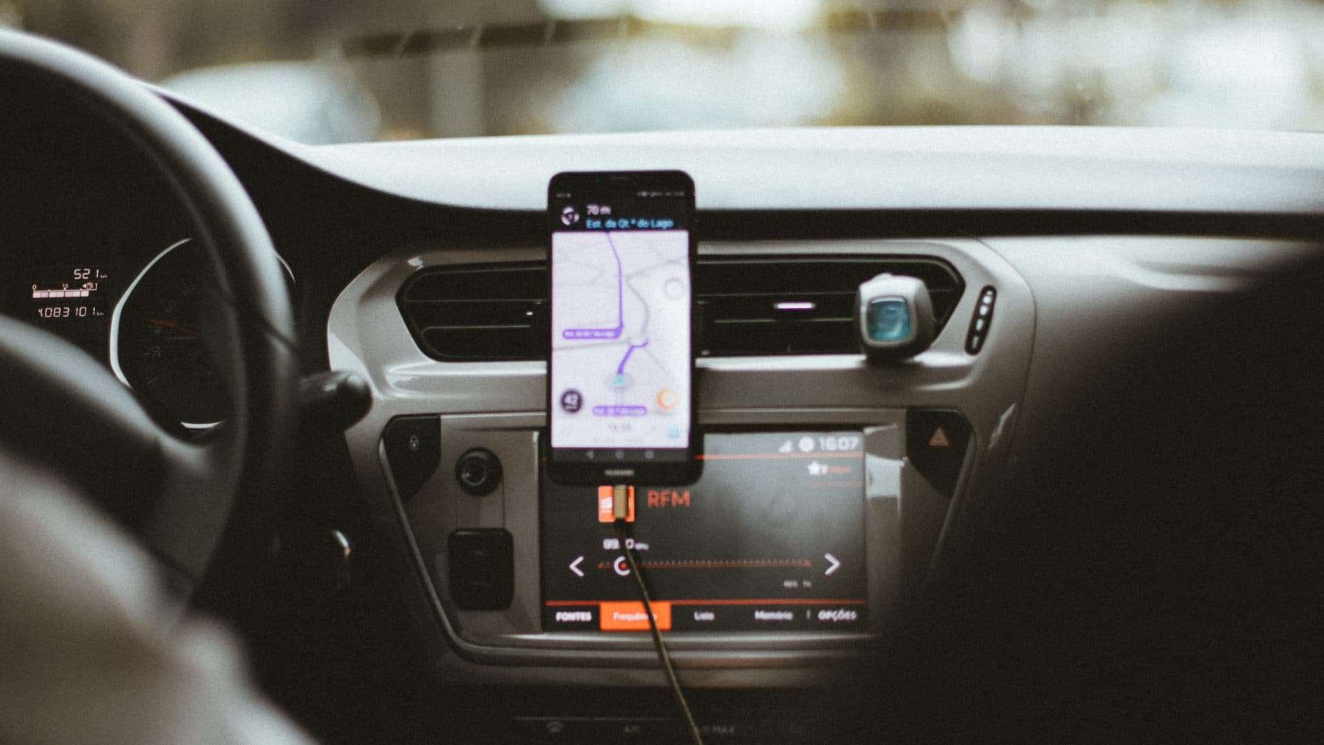 Celular disposto perto do painel de um carro mostrando a tela durante uma viagem no aplicativo Uber