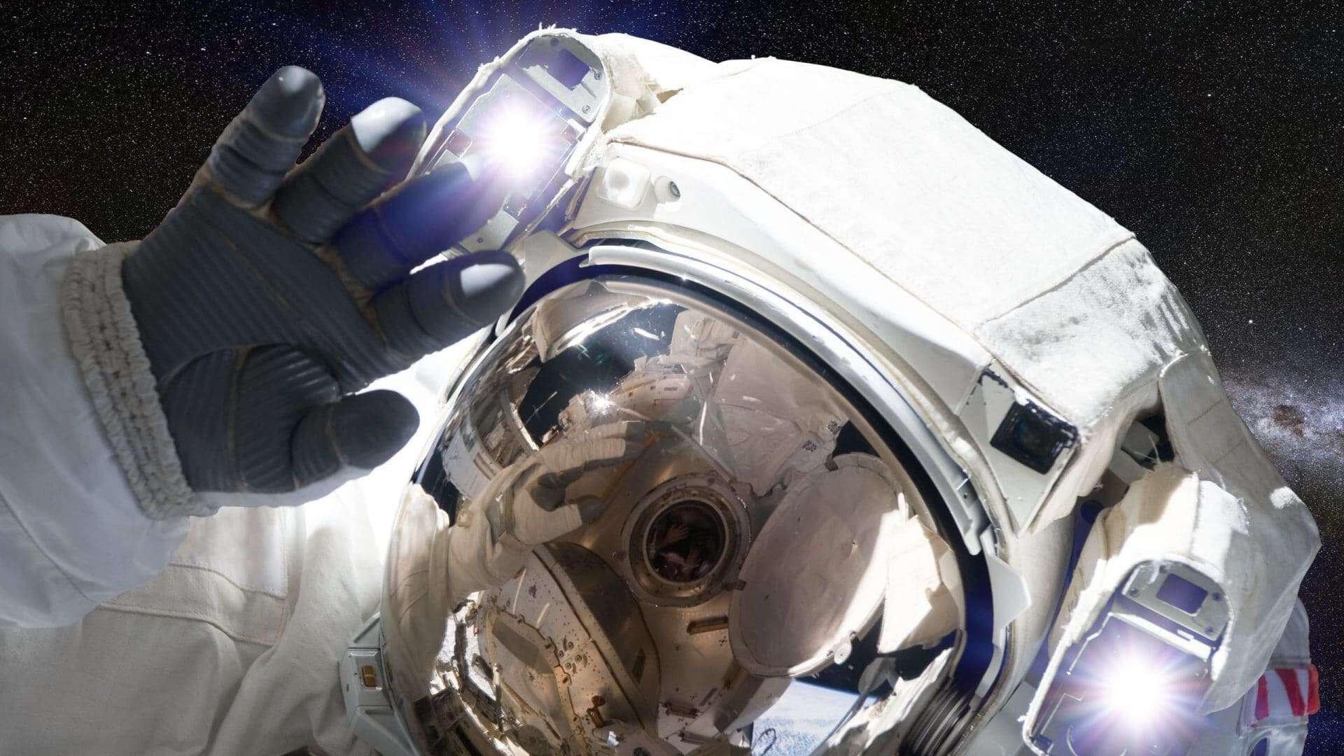 Imagem mostra um astronauta, em traje espacial completo, flutuando no espaço e acenando para a câmera