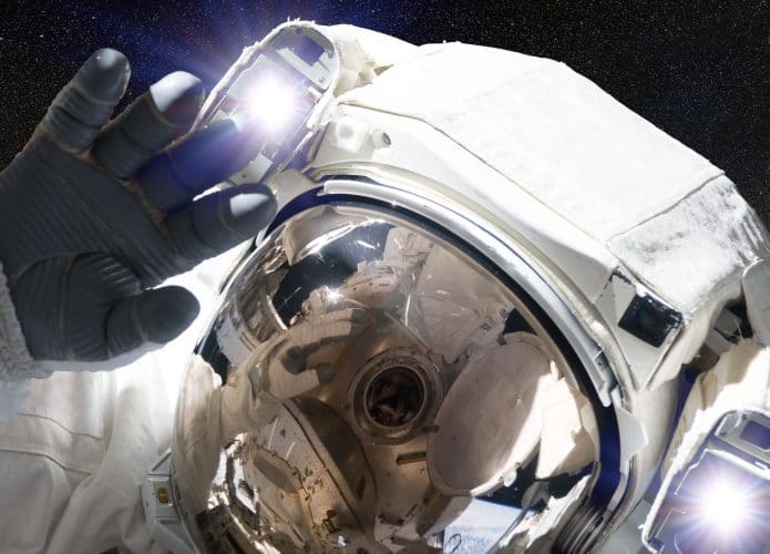 Imagem mostra um astronauta, em traje espacial completo, flutuando no espaço e acenando para a câmera