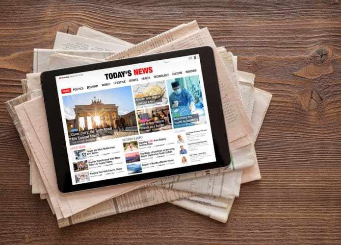 Tablet com site de notícias aberto, em cima de pilha de jornais