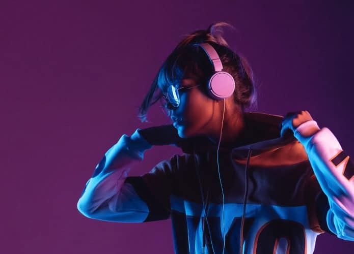 Menina ouvindo música com fone de ouvido em imagem com fundo roxo