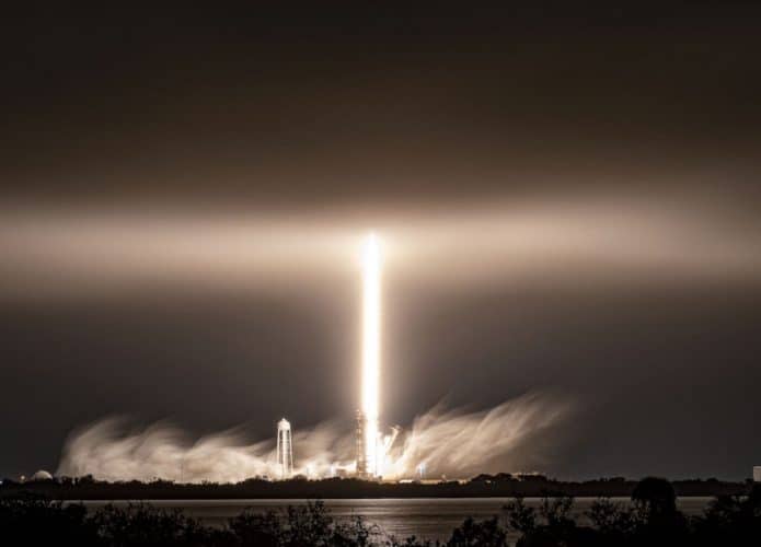 Imagem mostra lançamento noturno de um foguete Falcon 9 em meio a nuvens baixas e neblina