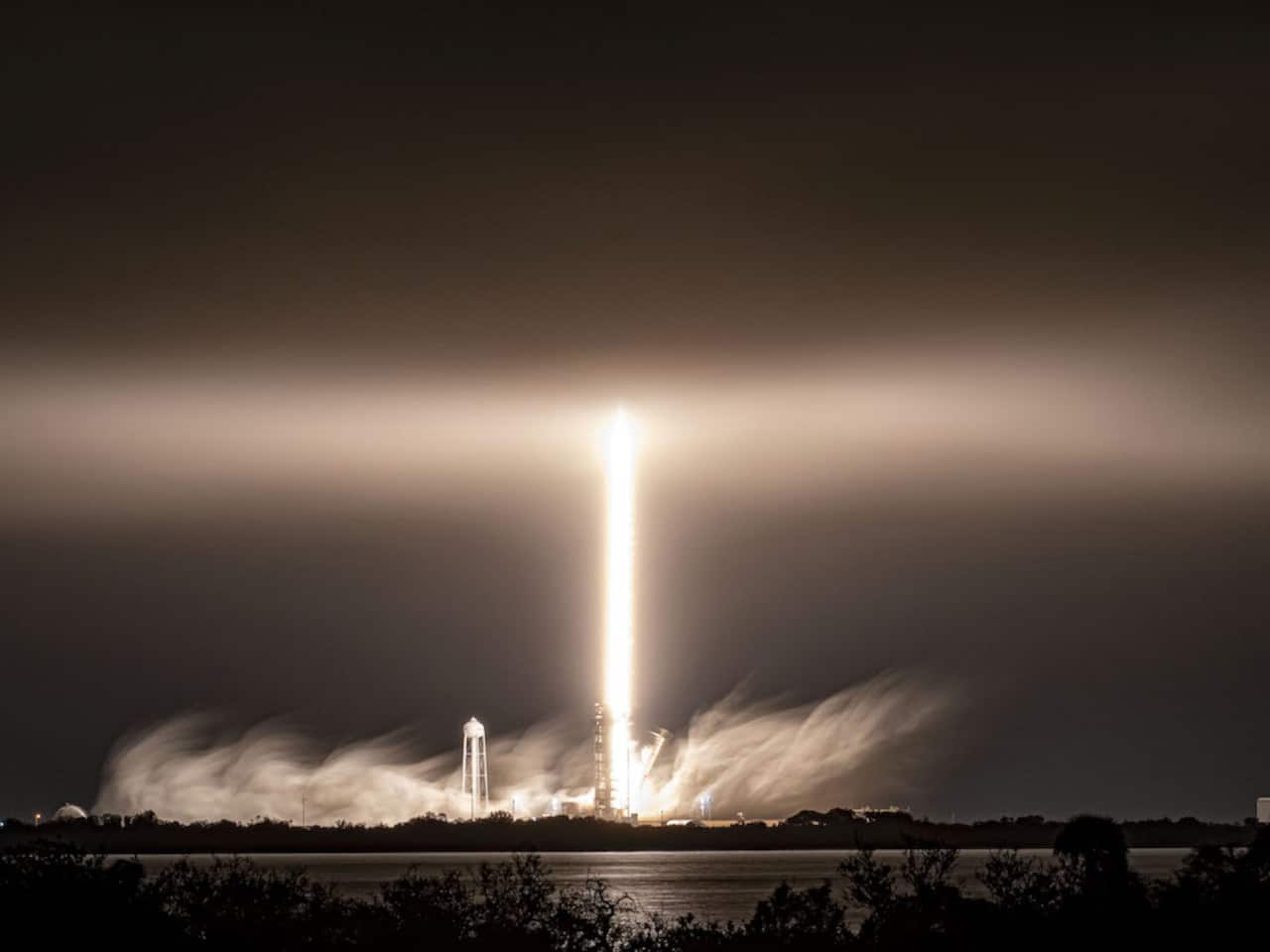 Imagem mostra lançamento noturno de um foguete Falcon 9 em meio a nuvens baixas e neblina