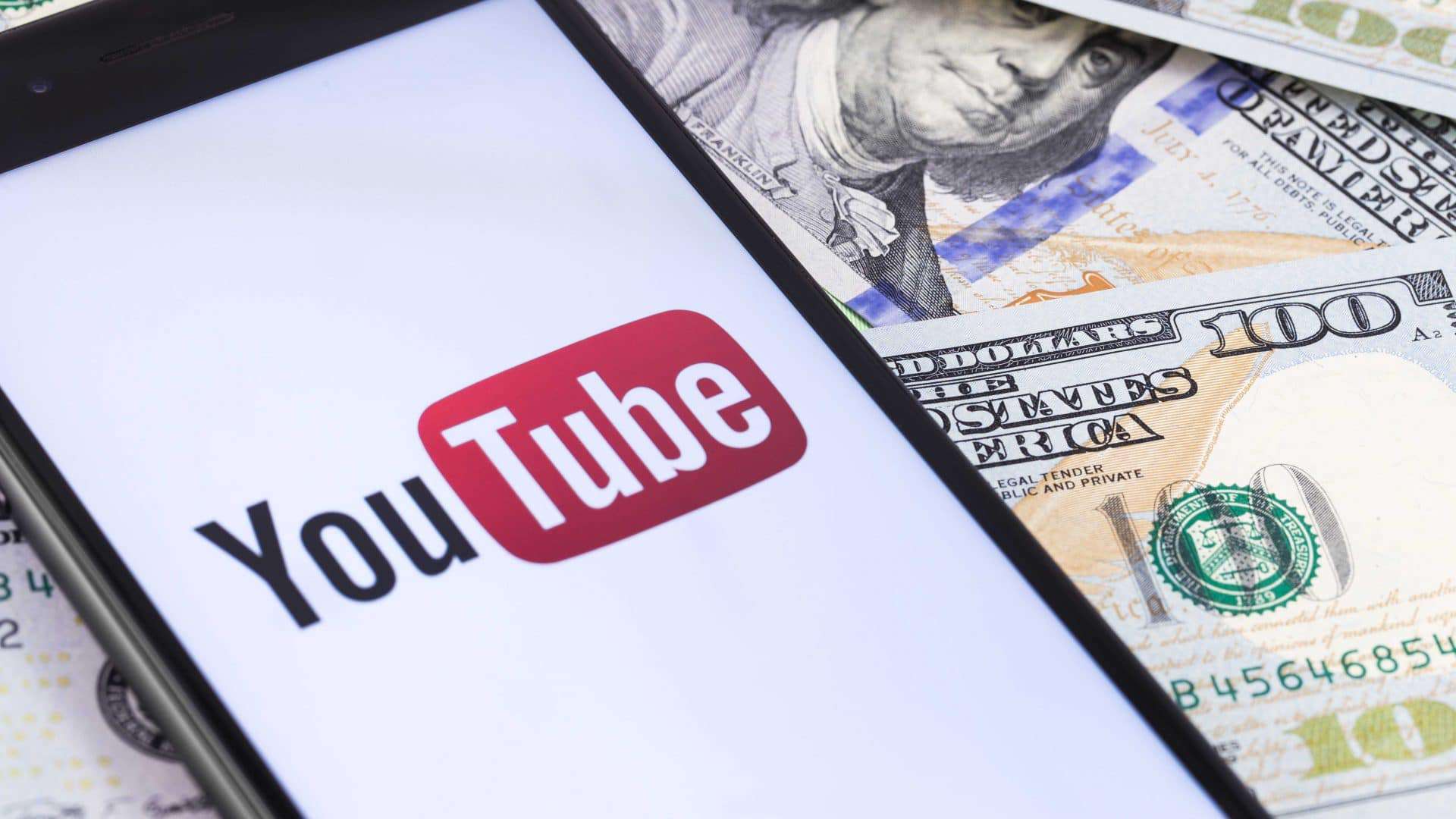 Logo do YouTube sendo exibido em smartphone e notas de dólar ao fundo