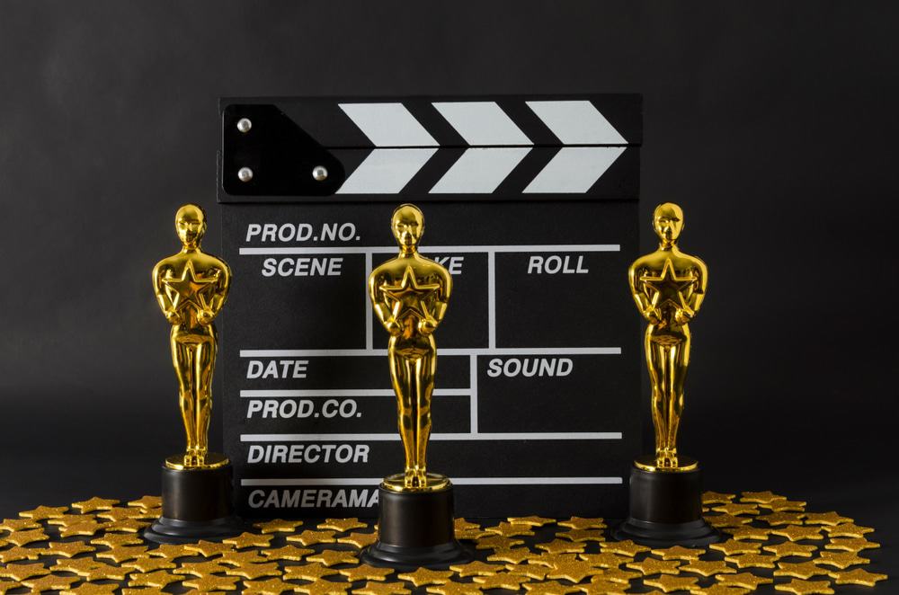 Imagem mostra várias estatuetas do Oscar alinhadas à frente de um claquete de cinema. Cerimônia de entrega do prêmio aos indicados ao Oscar será presencial, segundo a Academia