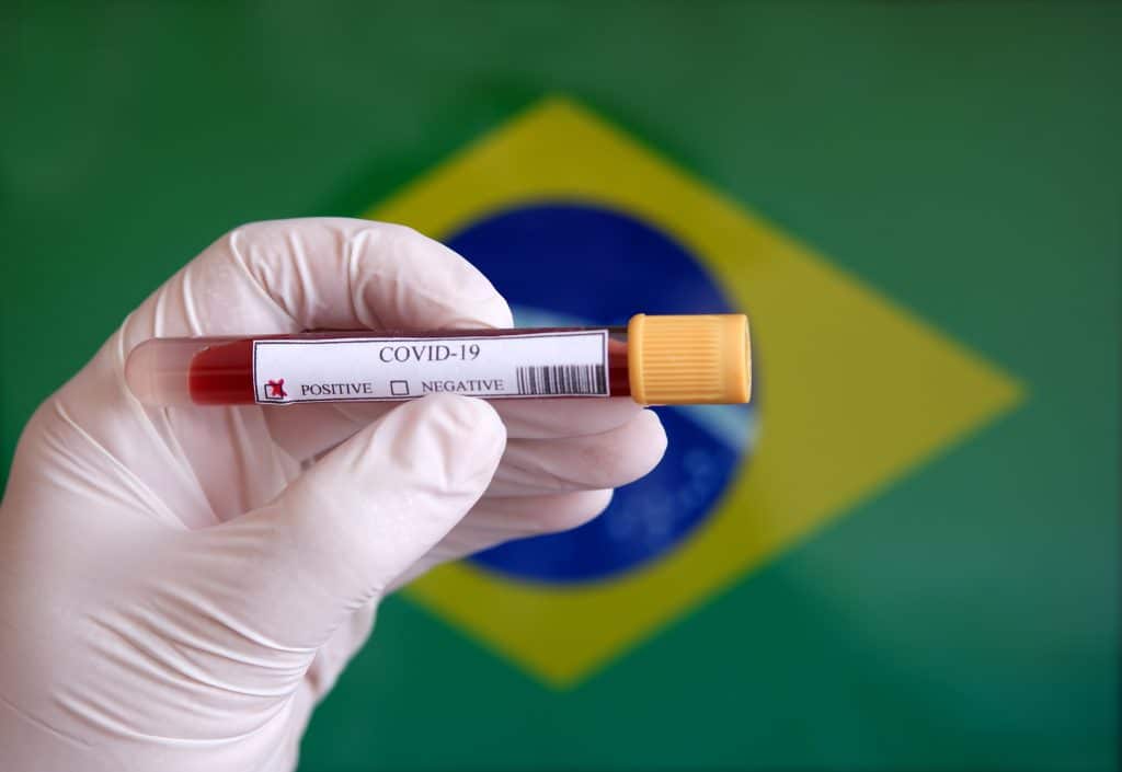 Amostra de sangue com resultado positivo para Covid-19 e ao fundo uma bandeira do Brasil