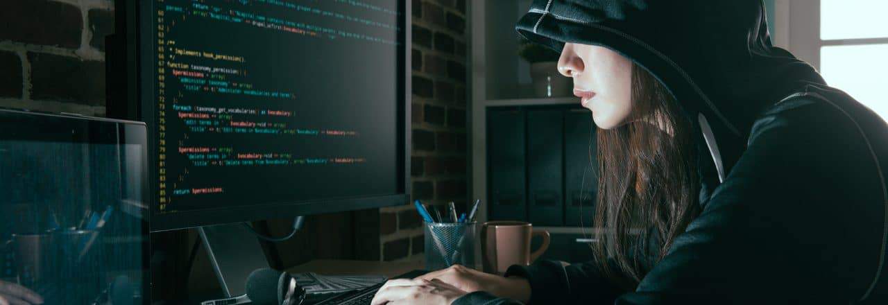 Imagem mostra uma mulher encapuzada, à frente de um computador, simbolizando um hacker