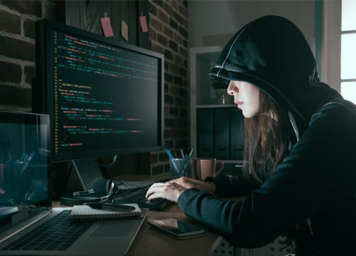 Imagem mostra uma mulher encapuzada, à frente de um computador, simbolizando um hacker