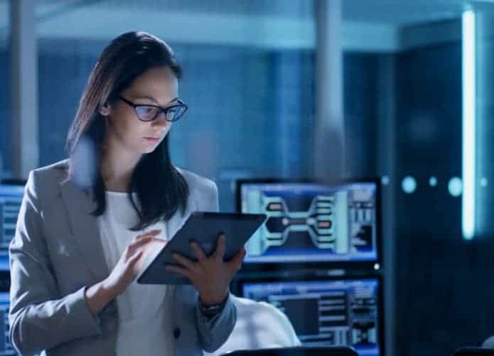 Imagem mostra uma mulher segurando um tablet dentro de uma sala com diversos computadores