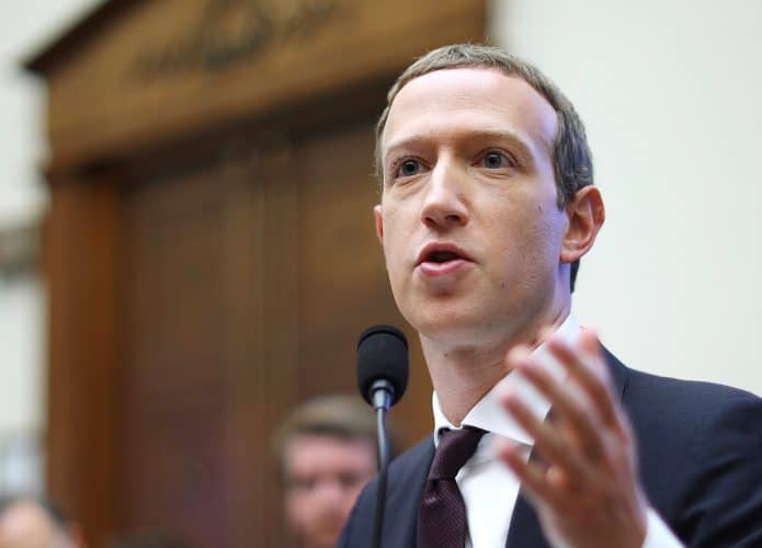 Inagem mostra o CEO do Facebook, Mark Zuckerberg, sentado em um acadeira de madeira, respondendo a perguntas durante uma audiência. Ele veste terno preto com gravata da mesma core está com o cabelo curto