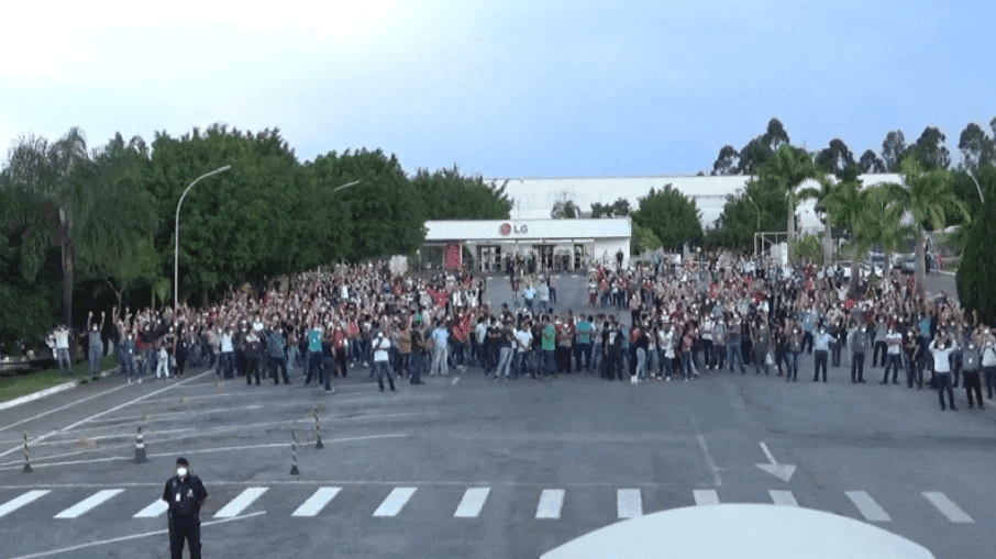 Foto mostra a fachada da fábrica da LG em Taubaté, com várias pessoas realizando manifestação à sua frente
