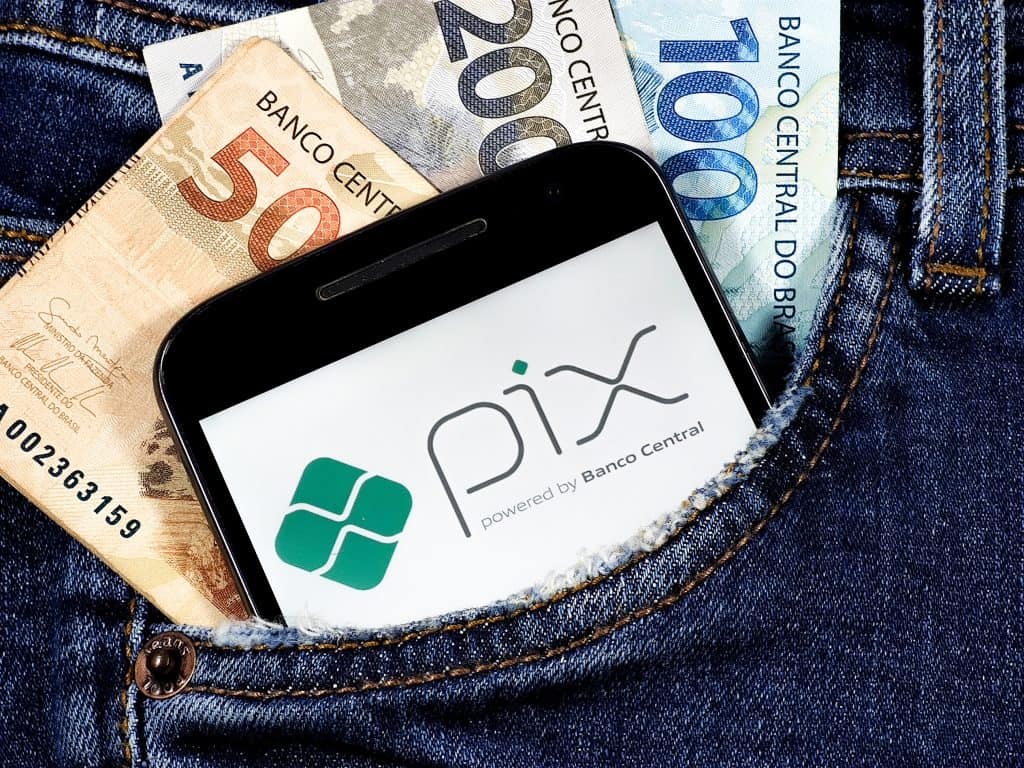 Celular com logo do Pix e notas de dinheiro em um bolso. 