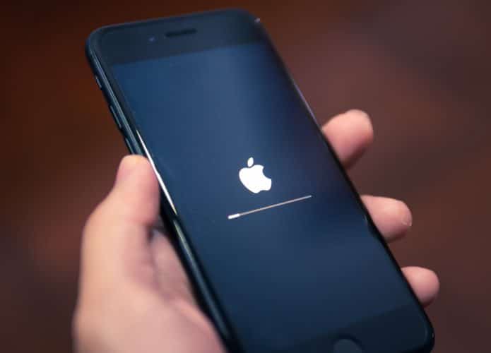 Imagem mostra uma mão segurando um iPhone, da Apple, com a tela mostrando o logo da mação, de carregamento inicial.