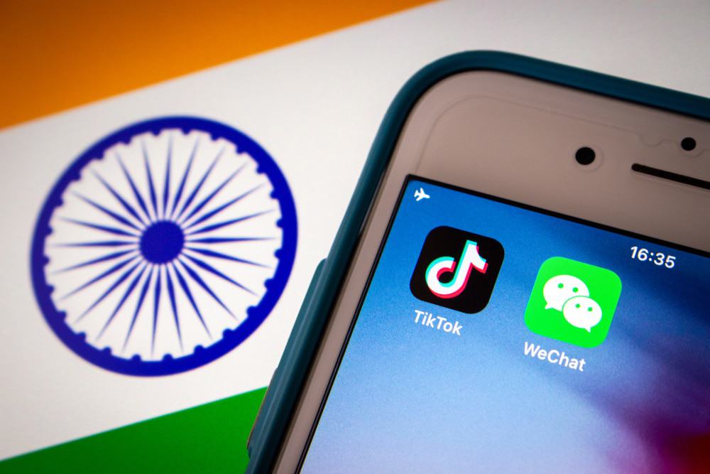 Imagem mostra, ao fundo, a bandeira da Índia; à frente um smartphone exibe dois ícones de aplicativos, entre eles o TikTok.