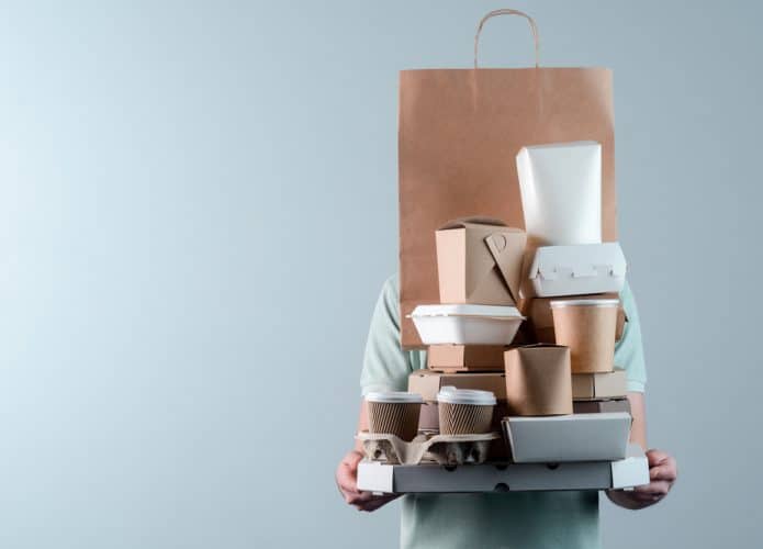 Imagem mostra uma pessoa carregando várias embalagens de delivery de comida.