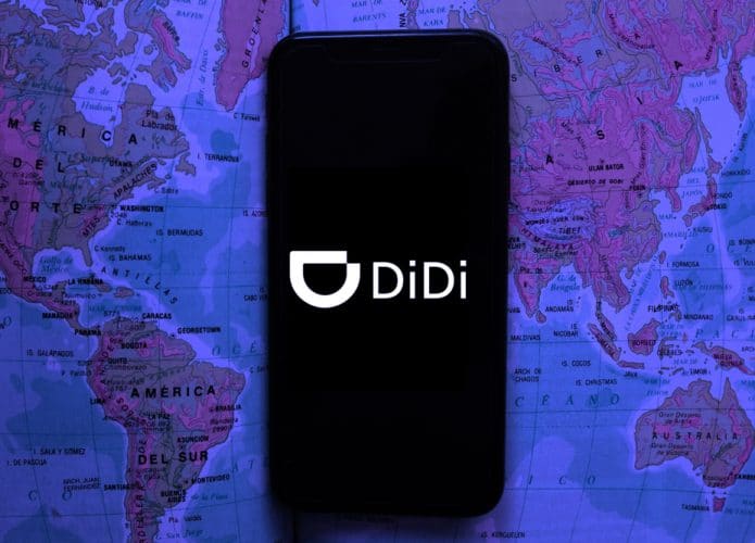 Smartphone exibe o logo do app didi chuxing, app de transporte Didi Chuxing na tela, ao fundo pode-se ver um mapa mundi