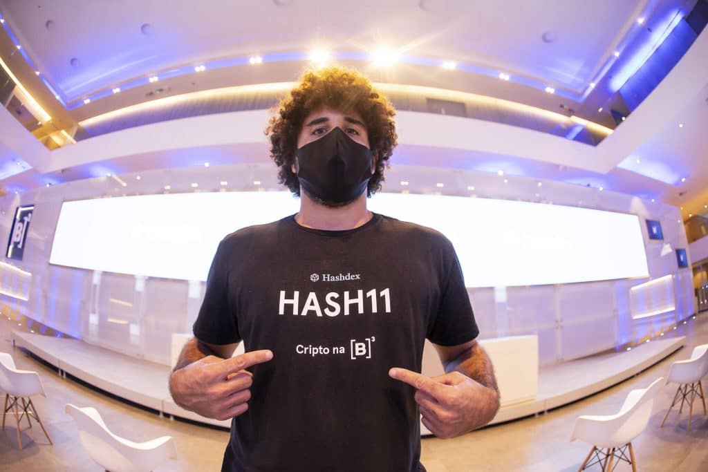 Imagem mostra um jovem com uma camiseta onde pode-se ler a palavra HASH11, sigla do ticker de negociação do primeiro fundo ETF de criptomoedas brasileiro