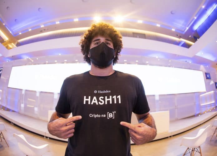 Imagem mostra um jovem com uma camiseta onde pode-se ler a palavra HASH11, sigla do ticker de negociação do primeiro fundo ETF de criptomoedas brasileiro