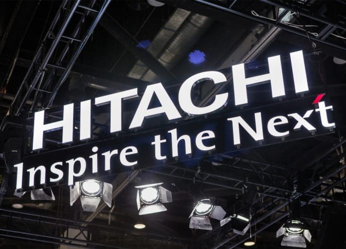 Logo da Hitachi em letra caixa, pendurado em um teto; abaixo o slogan Inspire the Next
