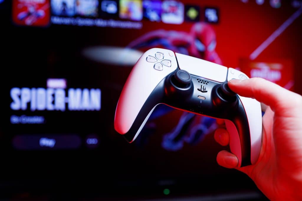 Uma mão segura o controle DualSense, do PlayStation 5, com o jogo "Marvel's Spider-Man: Miles Morales" sendo reproduzido em uma TV ao fundo