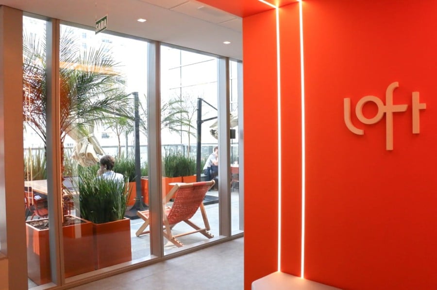Imagem mostra a entrada do escritório da startup Loft, com o logotipo da empresa na parede laranja.
