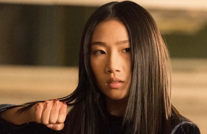 Imagem mostra a atriz Olivia Luang, em pose de luta para sua personagem na série 