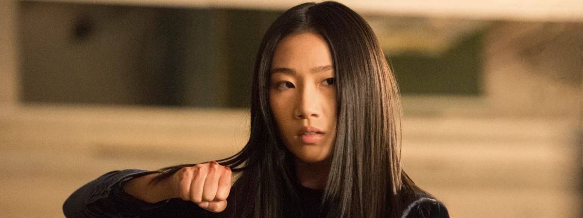 Imagem mostra a atriz Olivia Luang, em pose de luta para sua personagem na série 