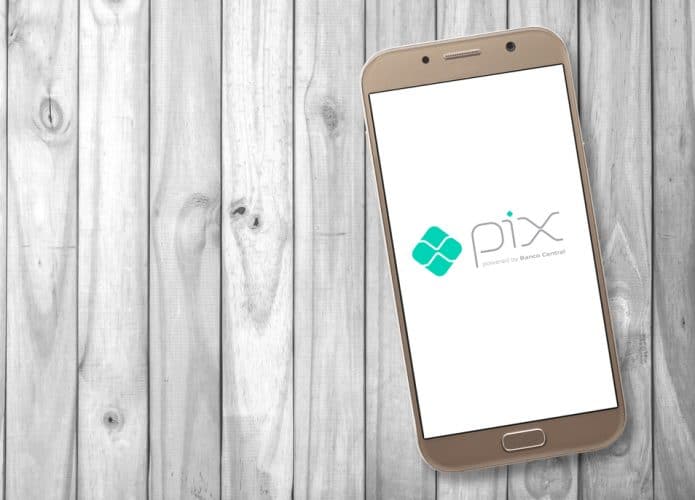 Sobre uma superfície de maneira, um smartphone que exibe na tela o logo do sistema de pagamento instantâneo do Banco Central, o PIX.