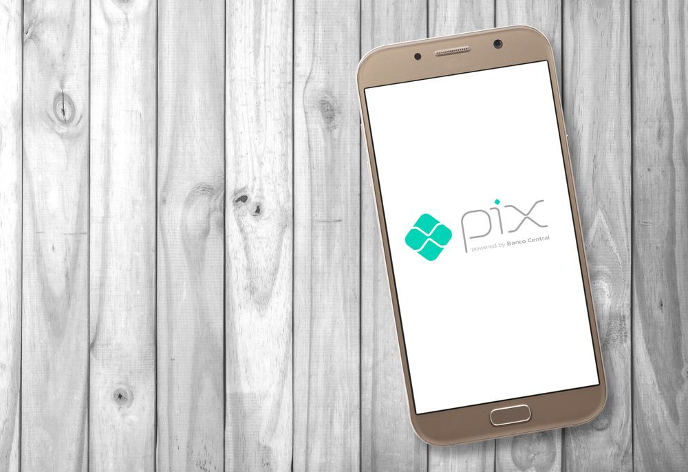 Sobre uma superfície de maneira, um smartphone que exibe na tela o logo do sistema de pagamento instantâneo do Banco Central, o PIX.