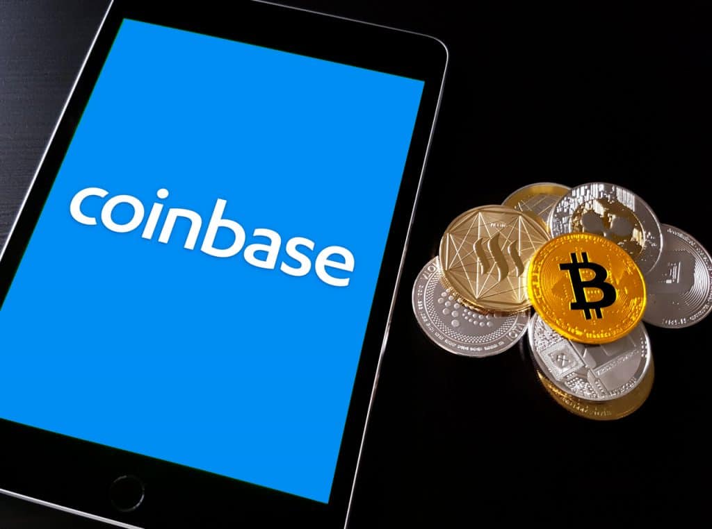 Logo da Coinbase em tablet ao lado de criptomoedas