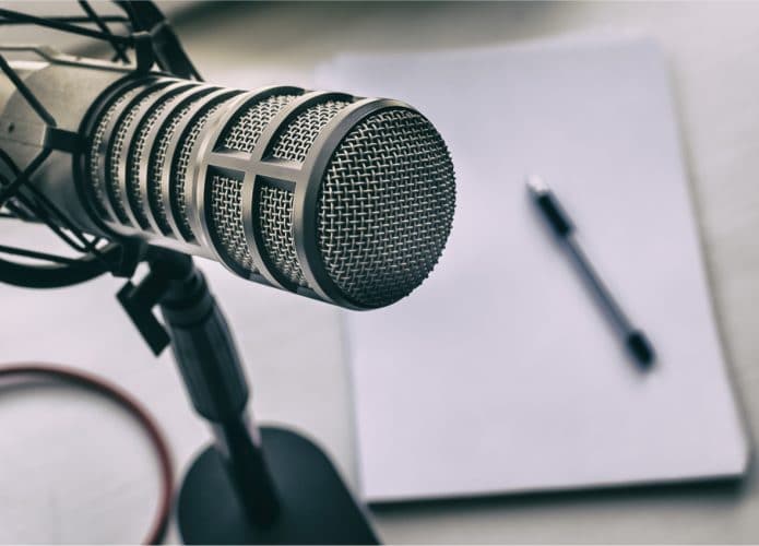 Spotify lança plataforma de assinatura para podcasts, competindo com a Apple. Na imagem: um microfone de podcast, com uma caneta e papel de anotações ao fundo
