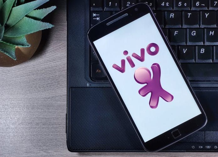 Em cima de uma superfície de madeira, aparece um teclado de notebook e, em cima dele, um smartphone com o logotipo da operadora Vivo na tela.
