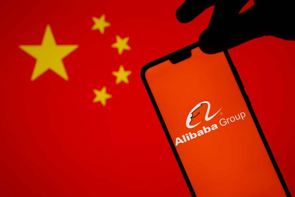 Logo do Alibaba exibido em smartphone e ao fundo uma bandeira da China