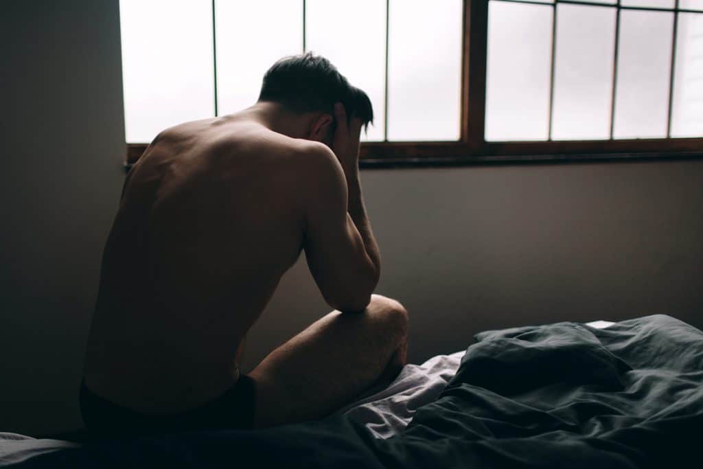 Homem sentado na cama com as mãos no rosto