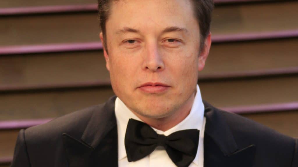 Elon Musk é exibido na imagem, usando gravata borboleta preta, paletó preto e camisa branca, em um evento de gala