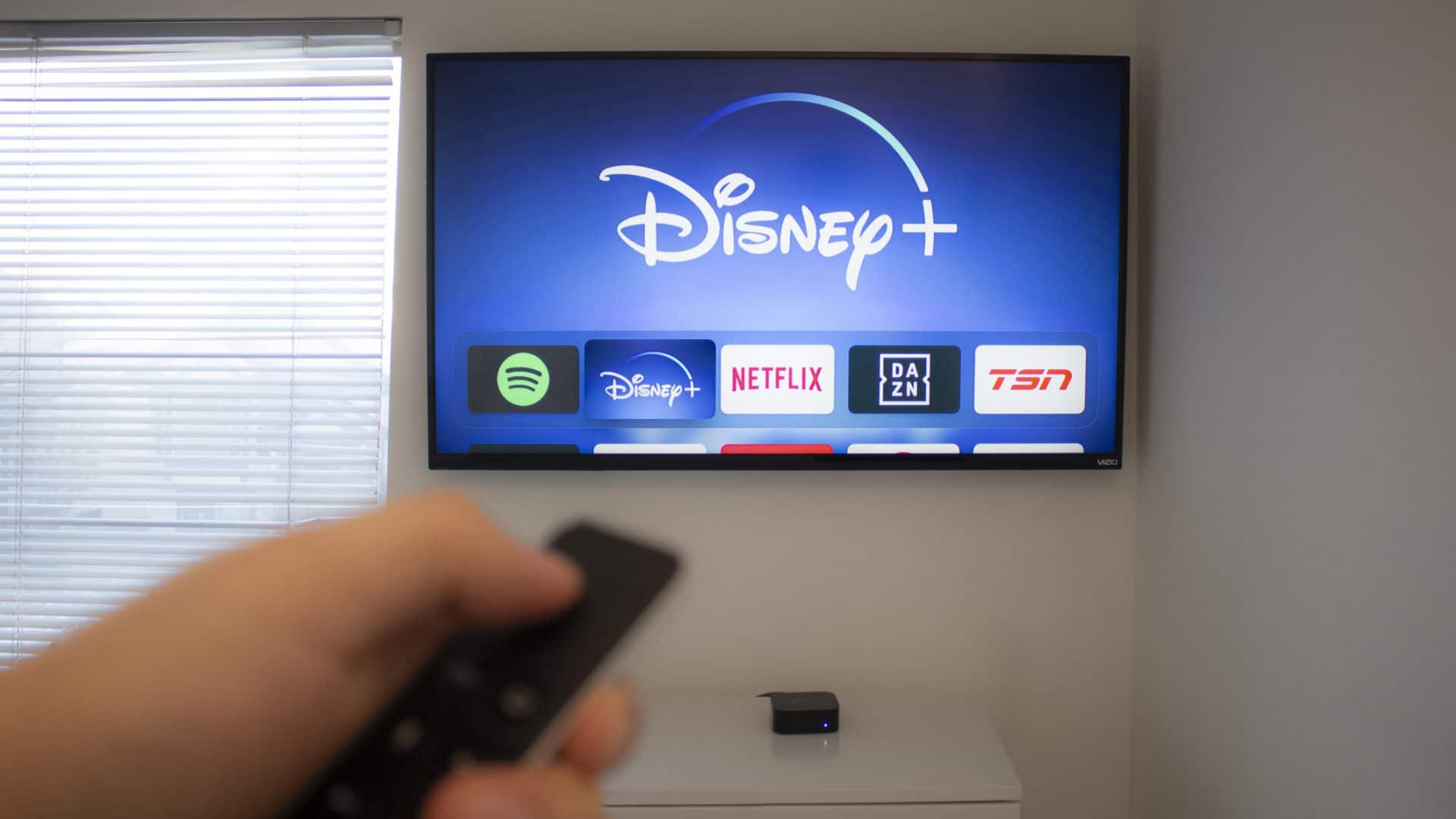 Pessoa segurando controle remoto e apontando para televisão com a plataforma de streaming Disney+ em destque