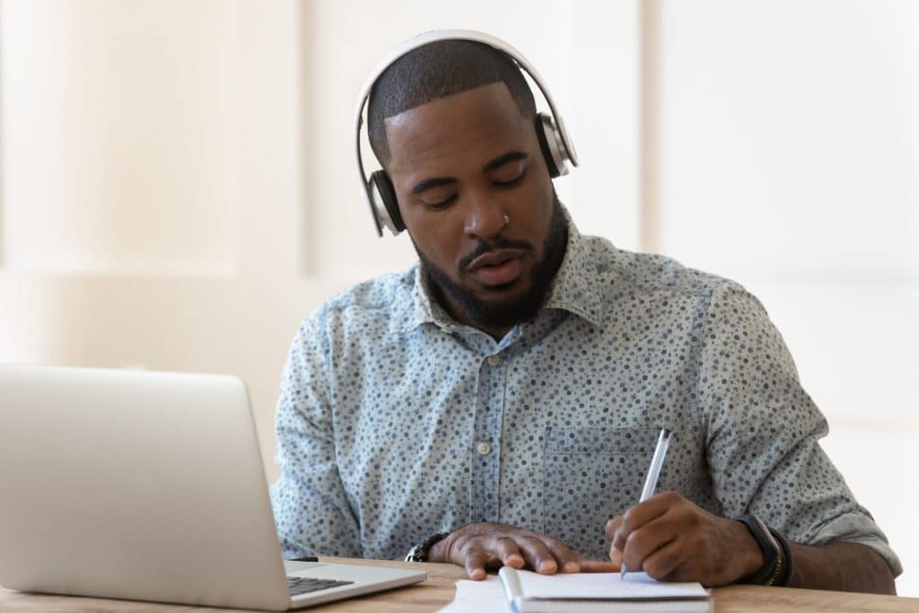 Homem sentado com fones de ouvido e fazendo anotações