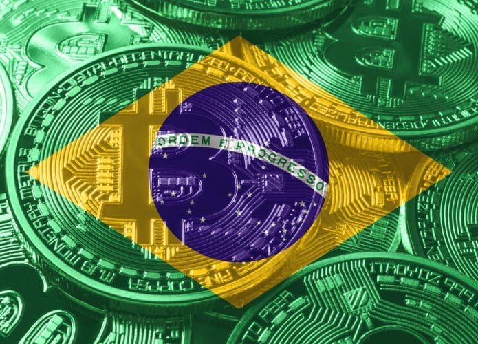 Imagem de uma bandeira do Brasil, com um bitcoin em relevo.