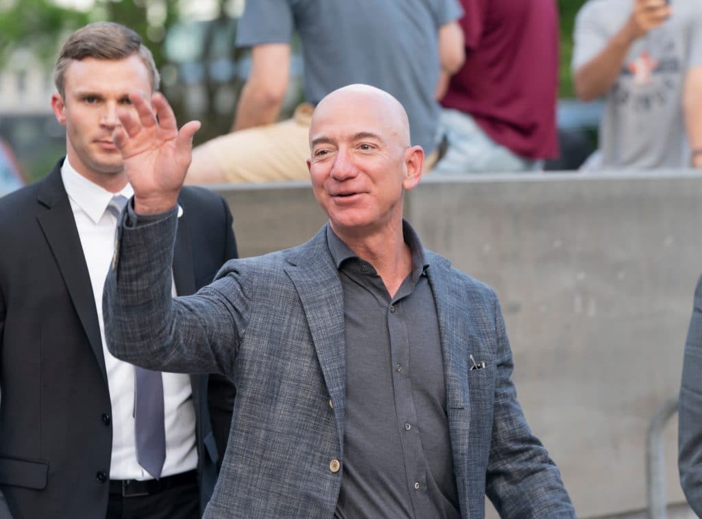 Imagem mostra Jeff Bezes, fundador da Amazon, acenando para às câmeras enquanto caminha em público.