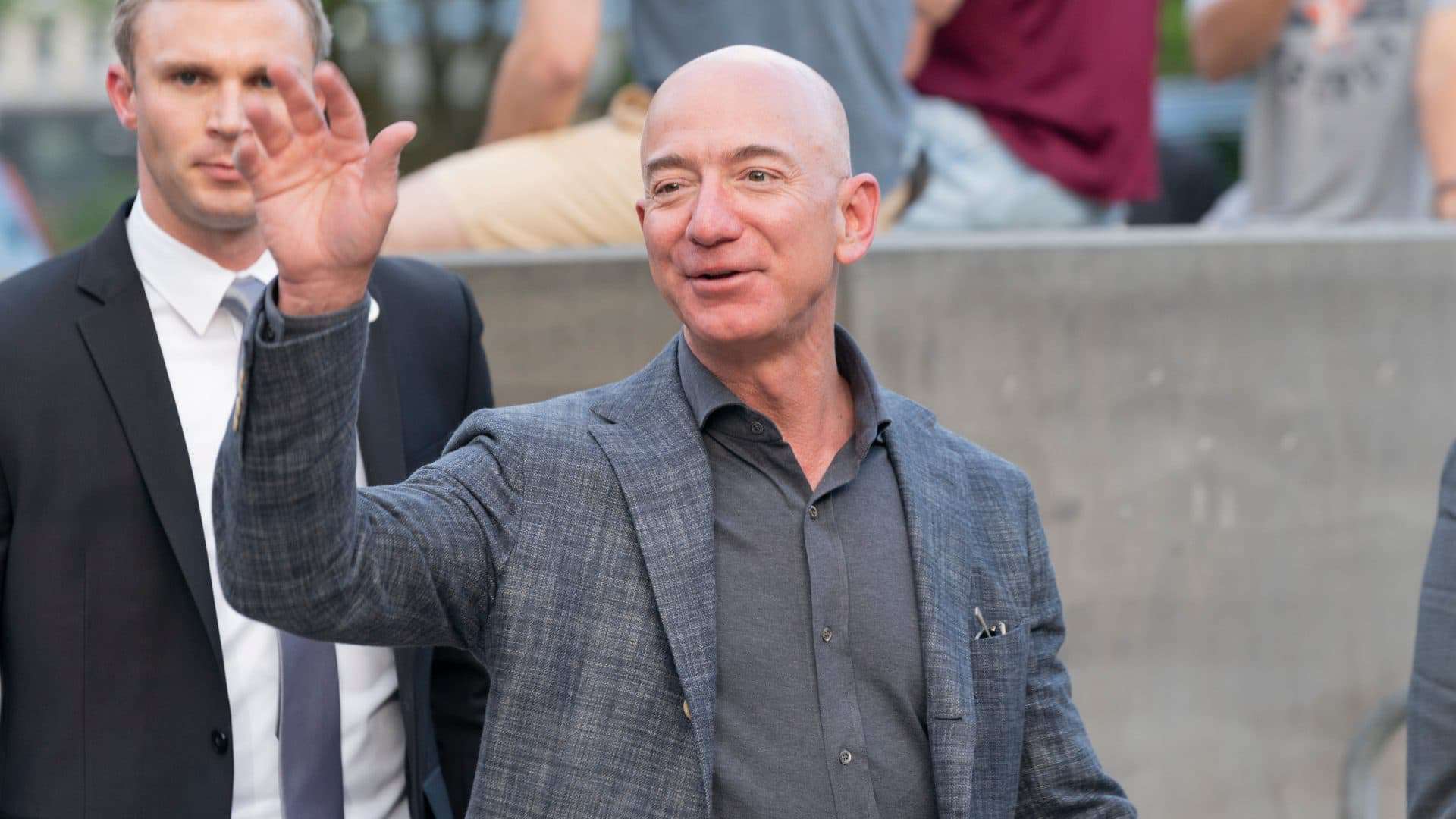 Imagem mostra Jeff Bezes, fundador da Amazon, acenando para às câmeras enquanto caminha em público.