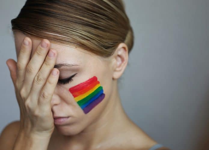 Mulher com semblante triste e uma bandeira LGBTQ desenhada em sua bochecha