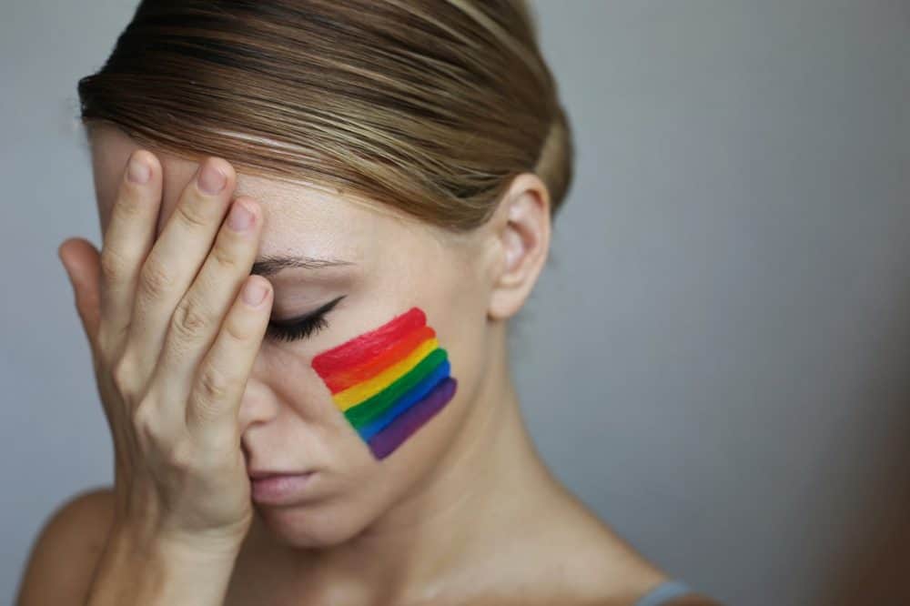 Mulher com semblante triste e uma bandeira LGBTQ desenhada em sua bochecha